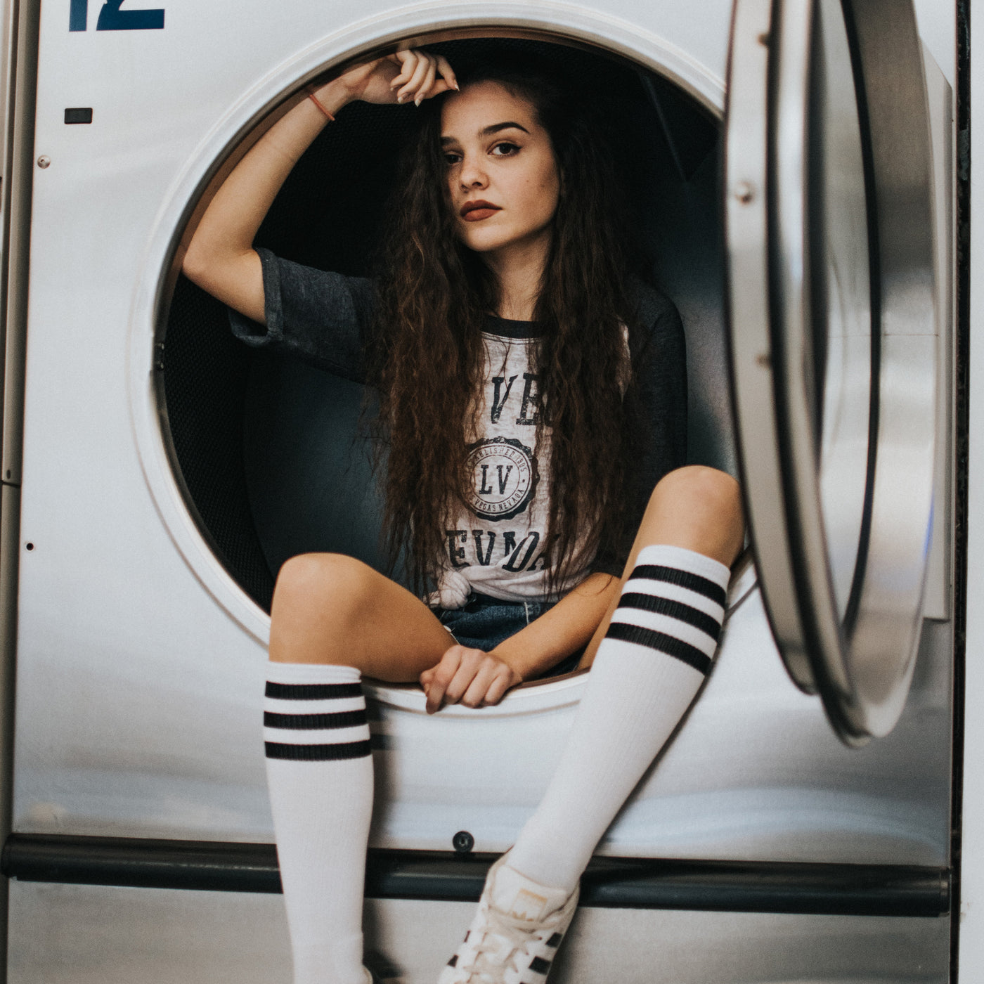 Girl sitting inside of washing machine wearing grunge clothing and white classic striped knee high socks american socks